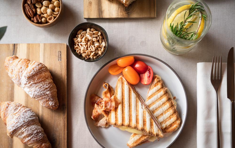 Breakfast with toast, croissants, cherry tomatoes, nuts, and infused water.